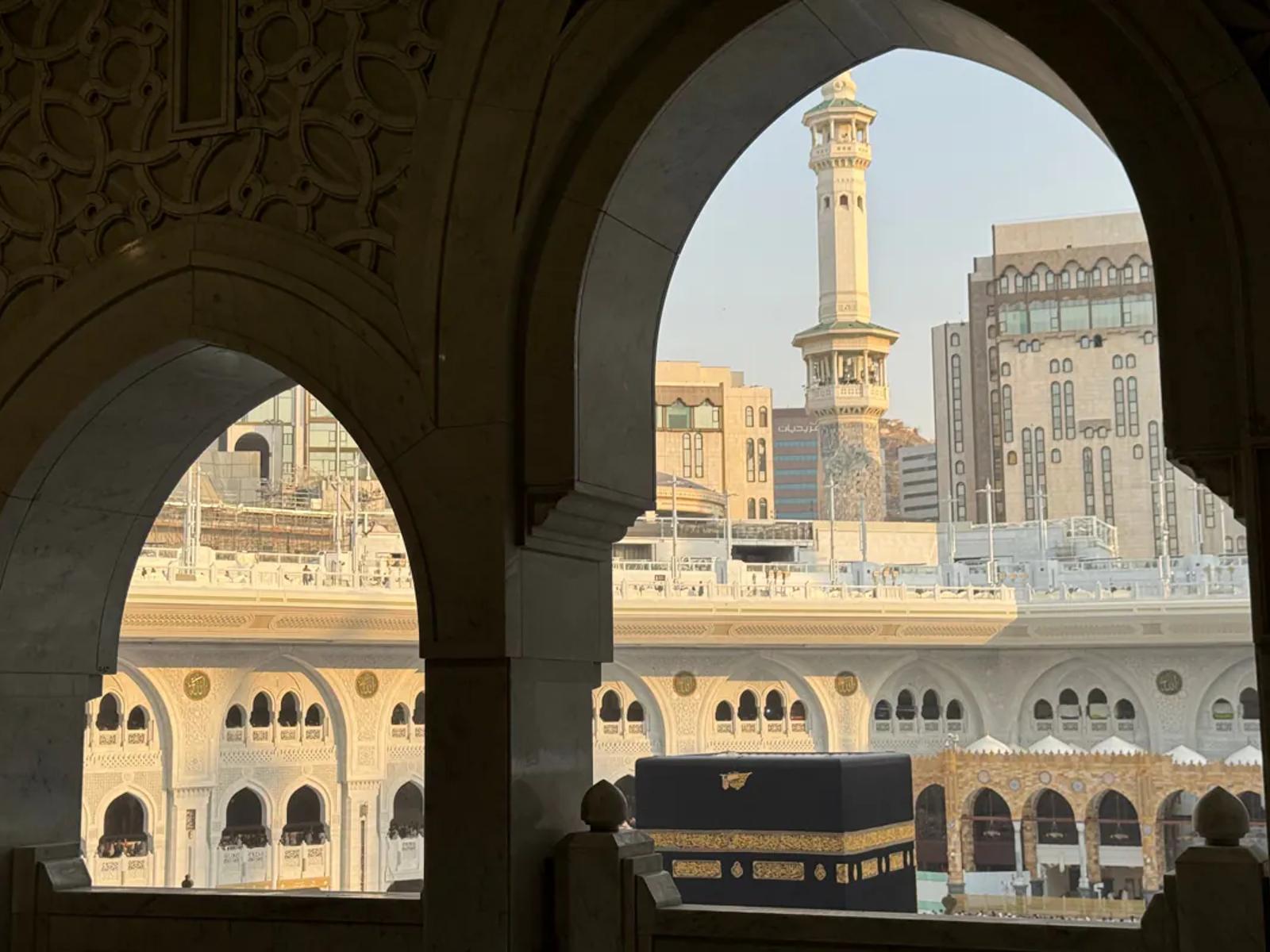 The Kaaba and a minaret framed by carved stone arches inside the Masjid al-Haram